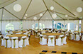 Large party tent with rented wooden tables and white chair covers accented with light green sashes
